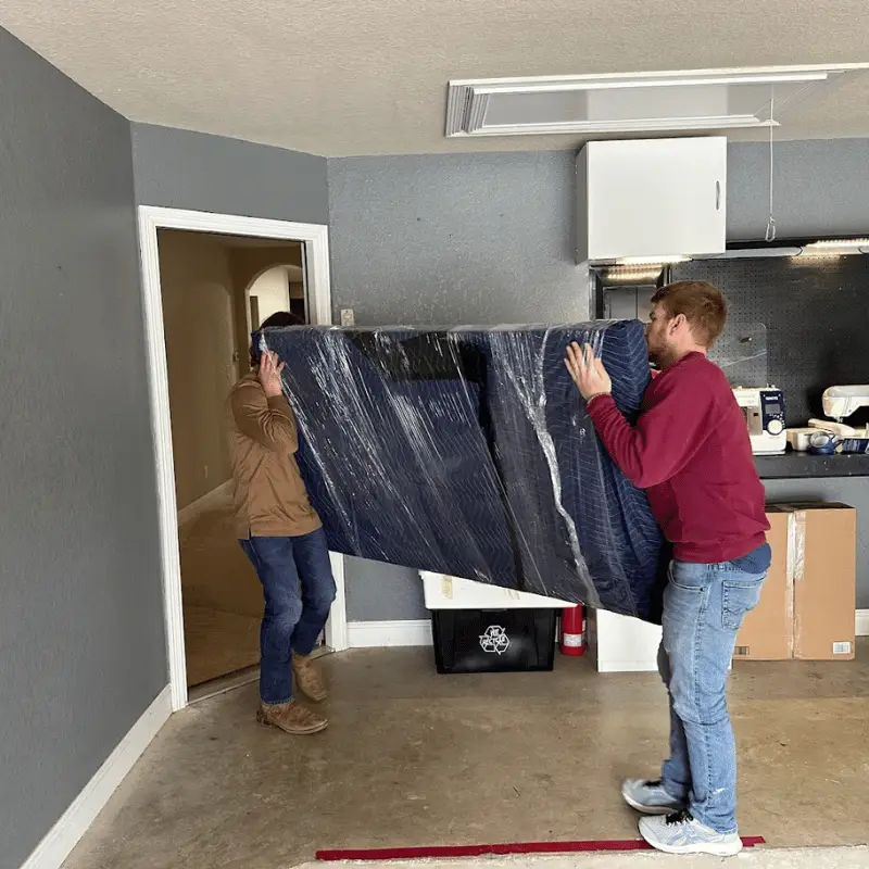 Full-Service vs. Self-Pack: Which Is Right for Your Move? 1 Movers carrying a wrapped piece of furniture out of a San Antonio home
